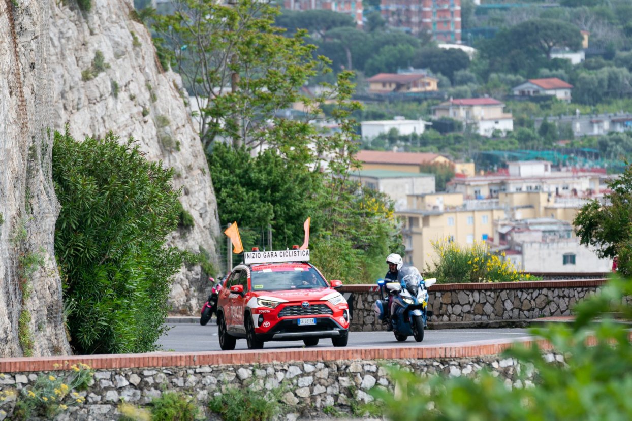Costiera amalfitana: la moto gialla della scorta, che segnala che il Giro sta arrivando,  a fianco dell’auto di inizio corsa dell’organizzazione